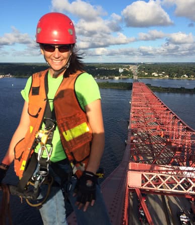 Female engineer in safety gear on a bridge construction site with water and sky background.