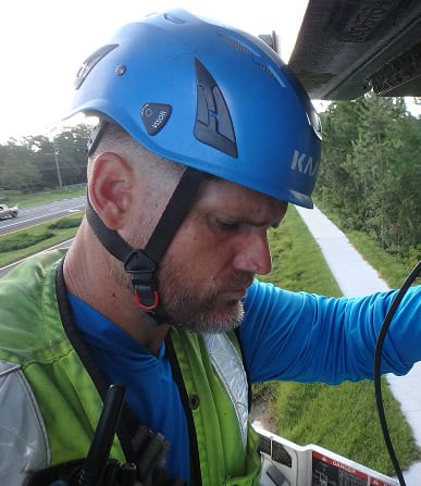 Utility worker inspecting equipment on a utility pole with safety gear and helmet.