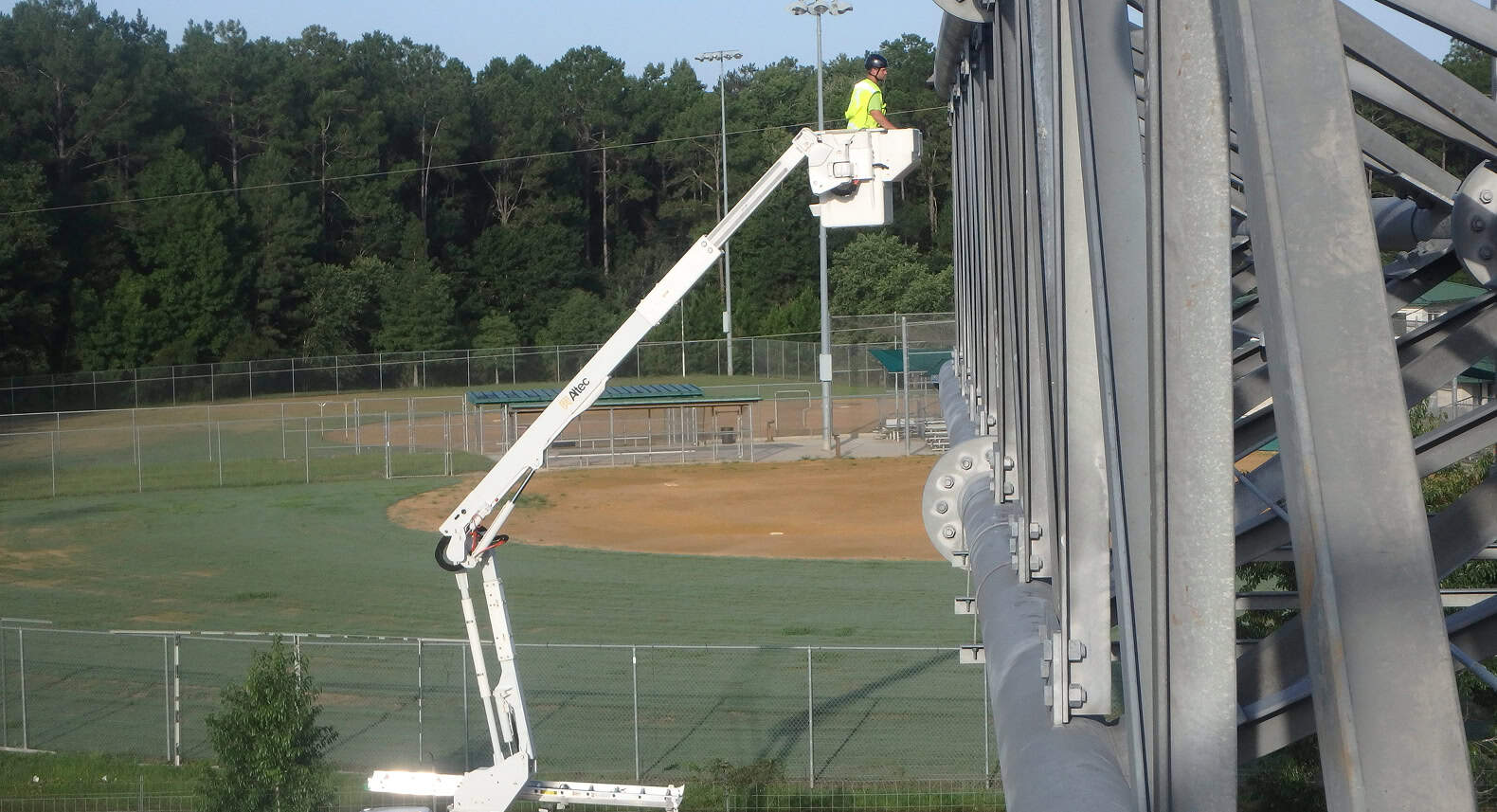 Elevated worker inspecting sports field from bucket truck for safety and maintenance.